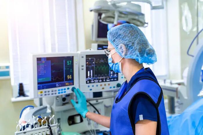 Personal médico monitoreando dispositivos en una sala de hospital. Se observa a un profesional de la salud, con bata y equipo de proteccion, operando una pantalla de monitoreo que muestra signos vitales y otros datos medicos.