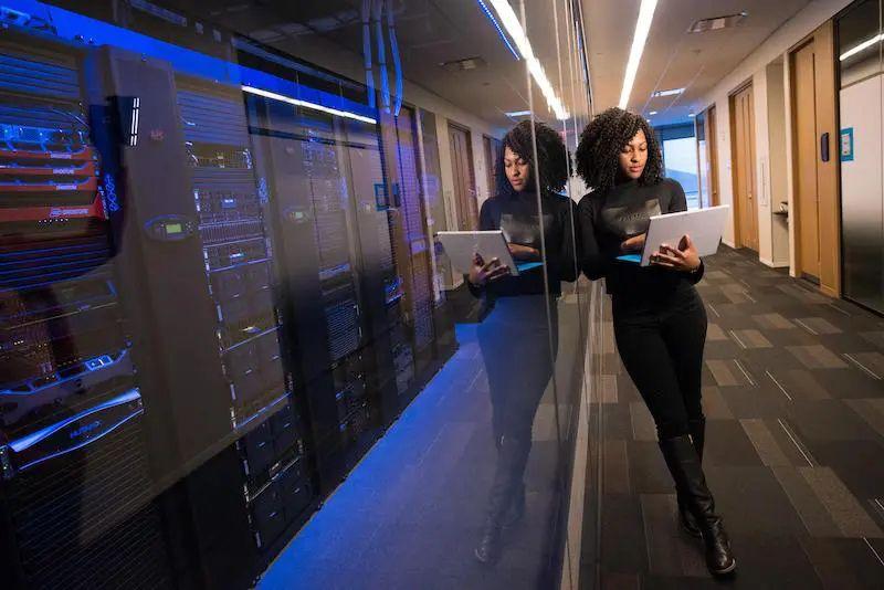 Mujer trabajando con una laptop frente a servidores en un centro de datos, representando la gestión y control de activos informáticos.