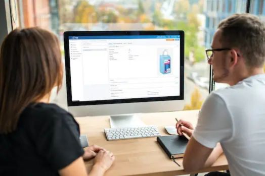 Dos personas revisando información en un monitor, destacando herramientas digitales para gestión de inventarios.