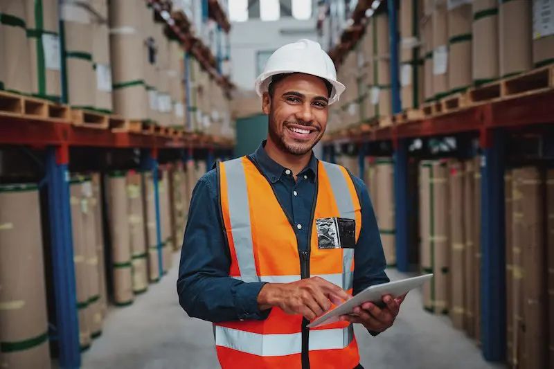 Trabajador sonriente en un almacén usando una tableta para gestionar el inventario de manera eficiente y en tiempo real.