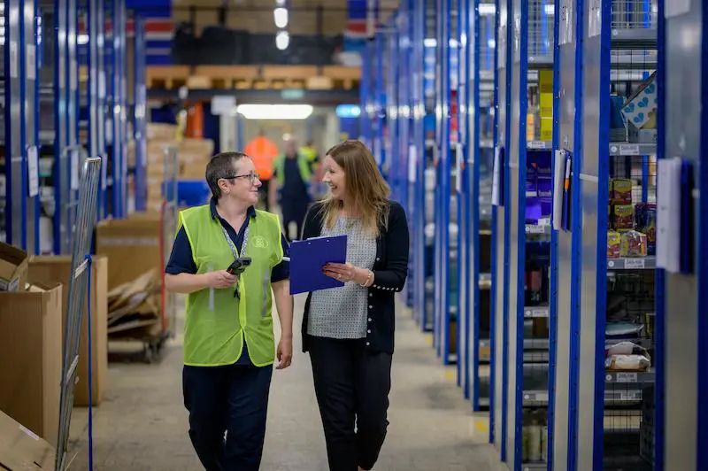 Dos trabajadores caminando por un almacén organizado, destacando las ventajas de una gestión eficiente del stock.