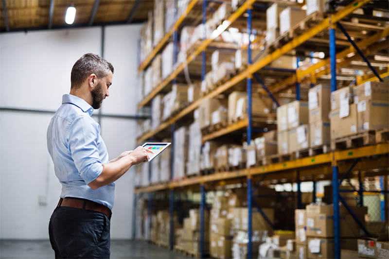 Worker using warehouse inventory software on a tablet in a warehouse setting