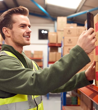 Trabajador escaneando el código de barras del inventario en los estantes usando un dispositivo digital o un teléfono móvil dentro del almacén