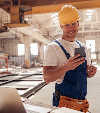 Trabajador en una nave industrial utilizando su móvil como escáner de código de barras para gestionar activos de manera eficiente.