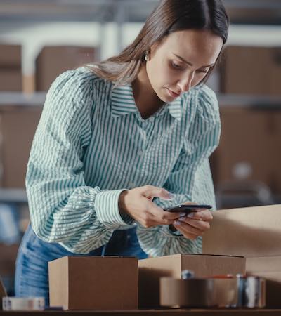 Trabajadora escaneando el código de barras de productos con su móvil para registrar activos en el almacén.