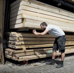 Empleado escaneando una pila de tablones de madera para gestionar el inventario en el almacén de Holzbau Bühlmann AG.