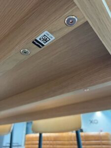 Detalle de un código QR de Timly debajo de una mesa, utilizado para la gestión digital del mobiliario en FlexOffice.