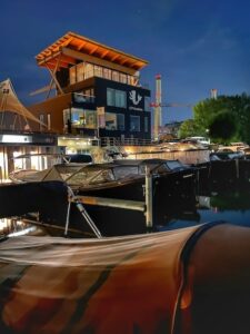 Vista nocturna del complejo Hafen & Hof con embarcaciones atracadas y el edificio iluminado junto al muelle.