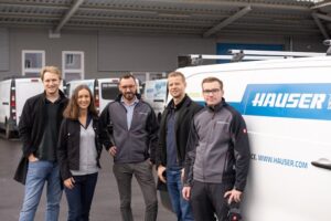 Cuatro empleados de HAUSER posando juntos frente a los vehículos de la empresa después de implementar Timly.