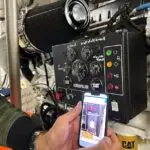 Manos de un miembro del equipo escaneando un código QR con un teléfono móvil delante de un panel de control técnico a bordo del barco.