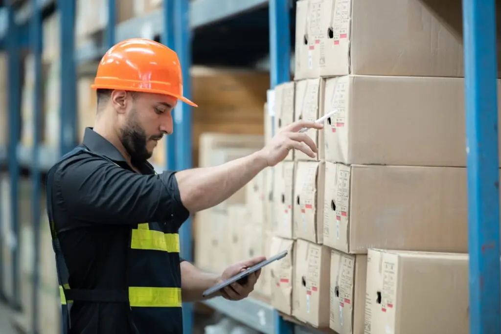 Trabajador revisando cajas en un almacén con una tablet durante un proceso de inventario rotativo.