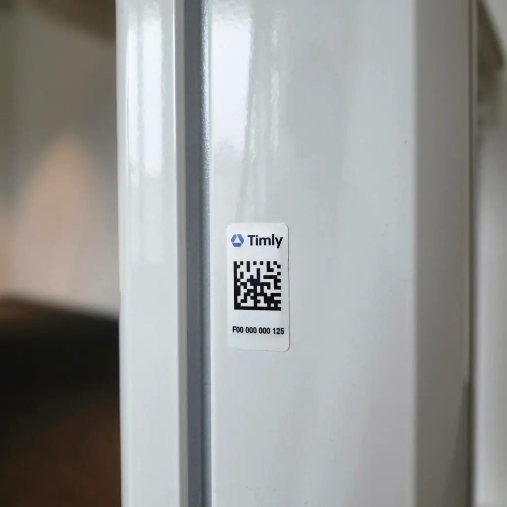 Etiqueta RFID de Timly con código QR adherida a una superficie metálica blanca.