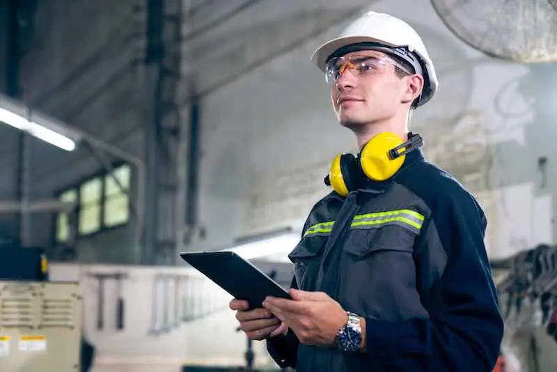Técnico de mantenimiento con casco y tablet revisando el plan de mantenimiento en una planta industrial.