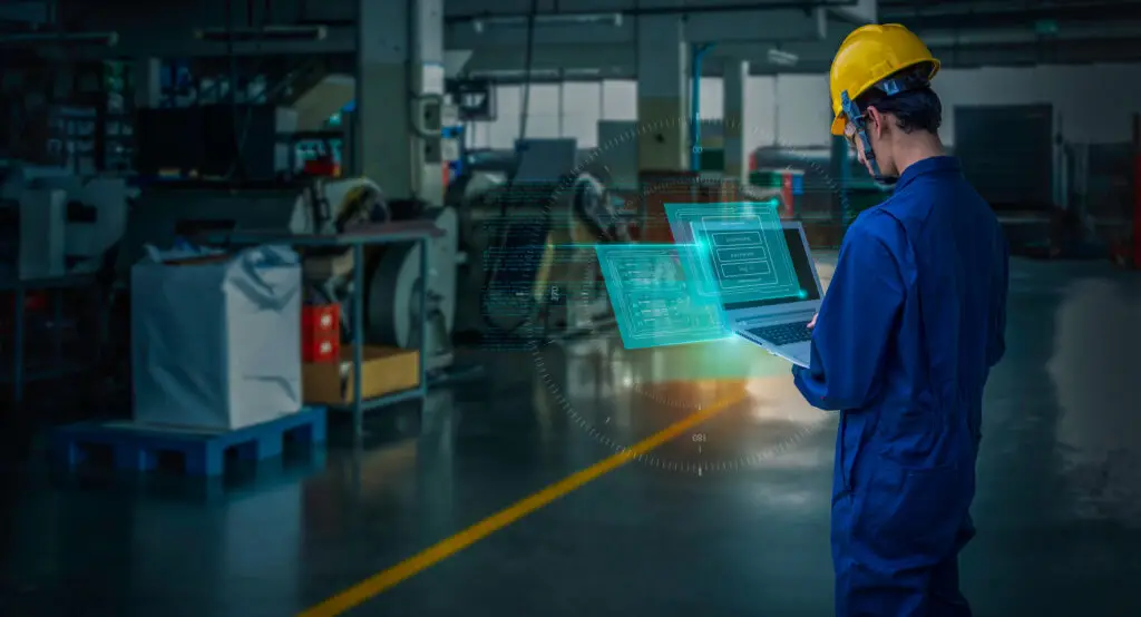 Trabajador supervisando el mantenimiento de maquinaria industrial con software en una fábrica.