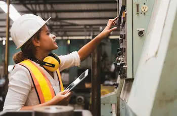 Operaria de mantenimiento industrial usando tablet con software para gestión de recursos materiales junto a máquina en planta de producción.