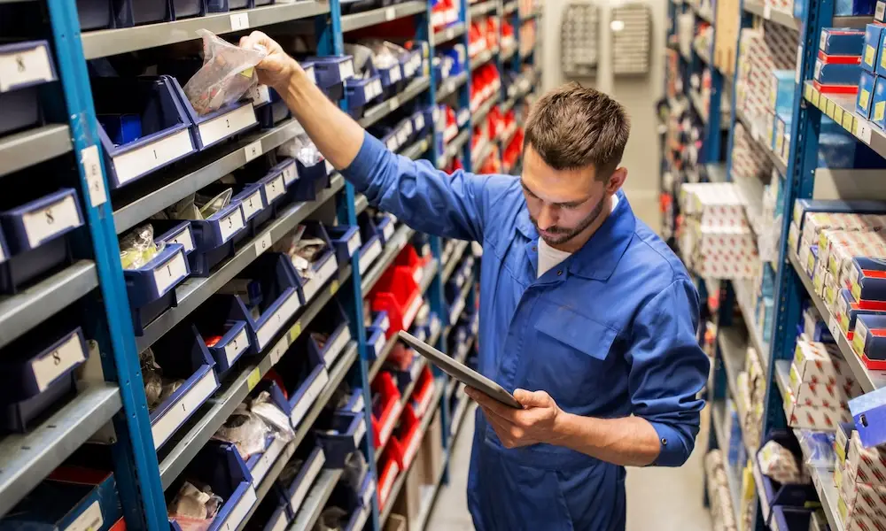L'image montre un employé en bleu de travail qui utilise le logiciel de gestion des stocks de Timly dans un entrepôt