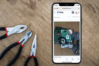 Herramientas manuales sobre la mesa y aplicación de Timly en el móvil para escanear códigos y gestionar el inventario de herramientas.