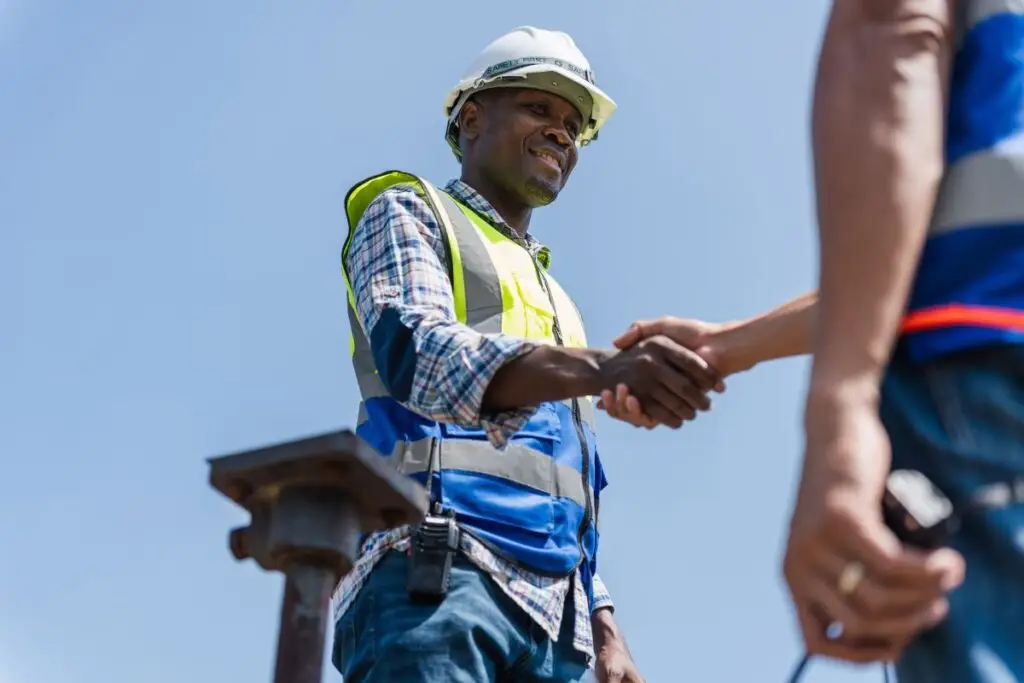 L'image montre un employé du secteur de la construction sur un chantier. Il serre la main d'un autre employé. Cette image illustre un article sur le PV de réception des travaux.