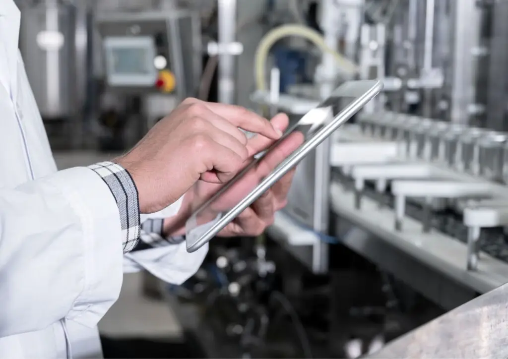 Técnico utilizando una tablet frente a una línea de producción para gestionar un plan de mantenimiento preventivo.