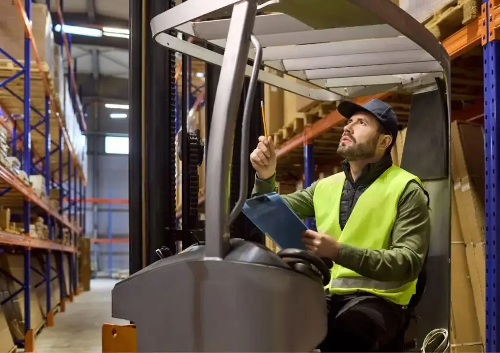 Technicien réalisant la vérification périodique des racks de stockage depuis une nacelle élévatrice dans un entrepôt, dans le contexte de la norme NF EN 16535.